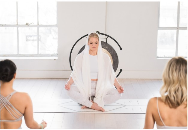 Piper Hogan Global Soul Yoga meditating with student in front of gong